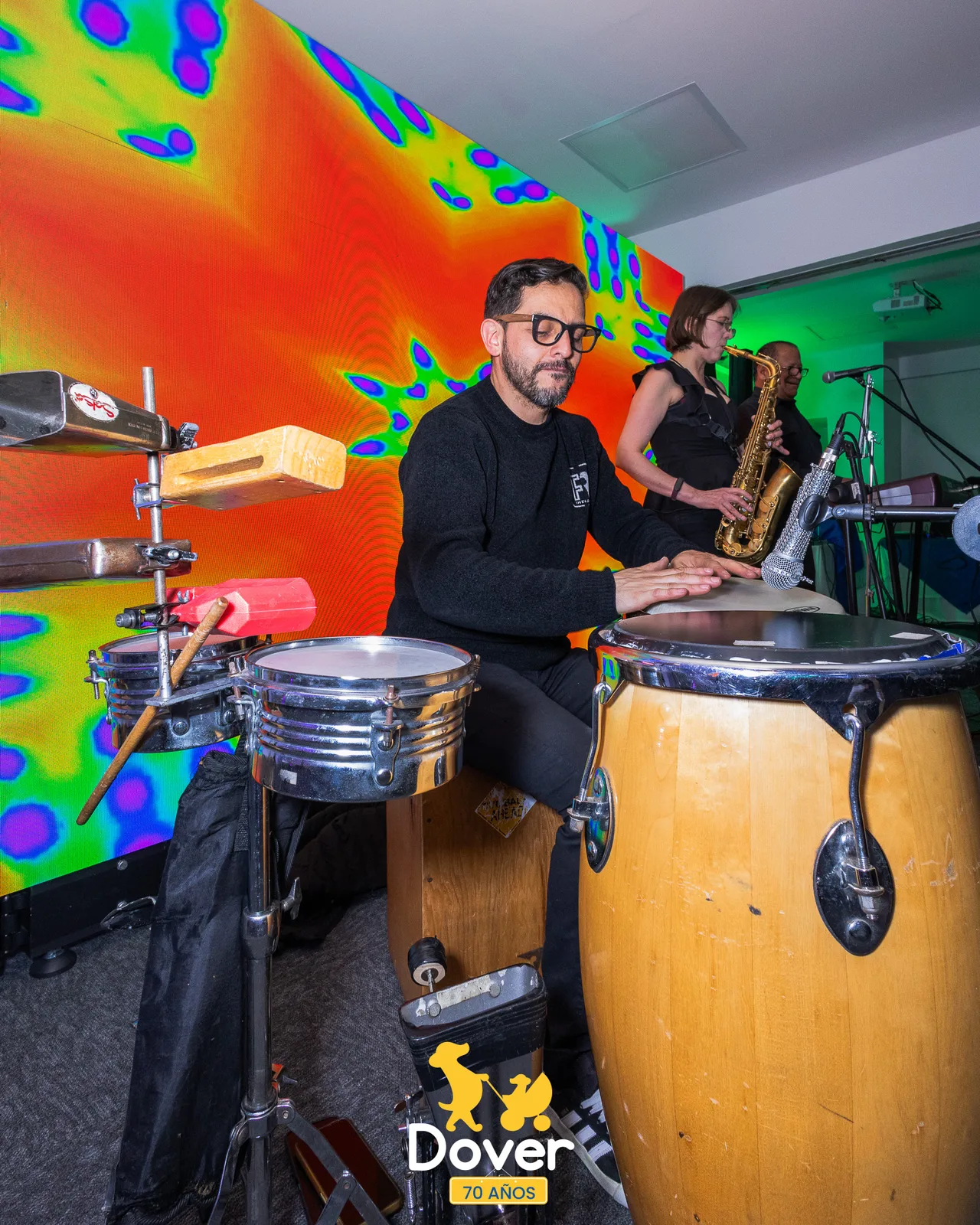 Músicos interpretan percusión frente a una pantalla de colores.